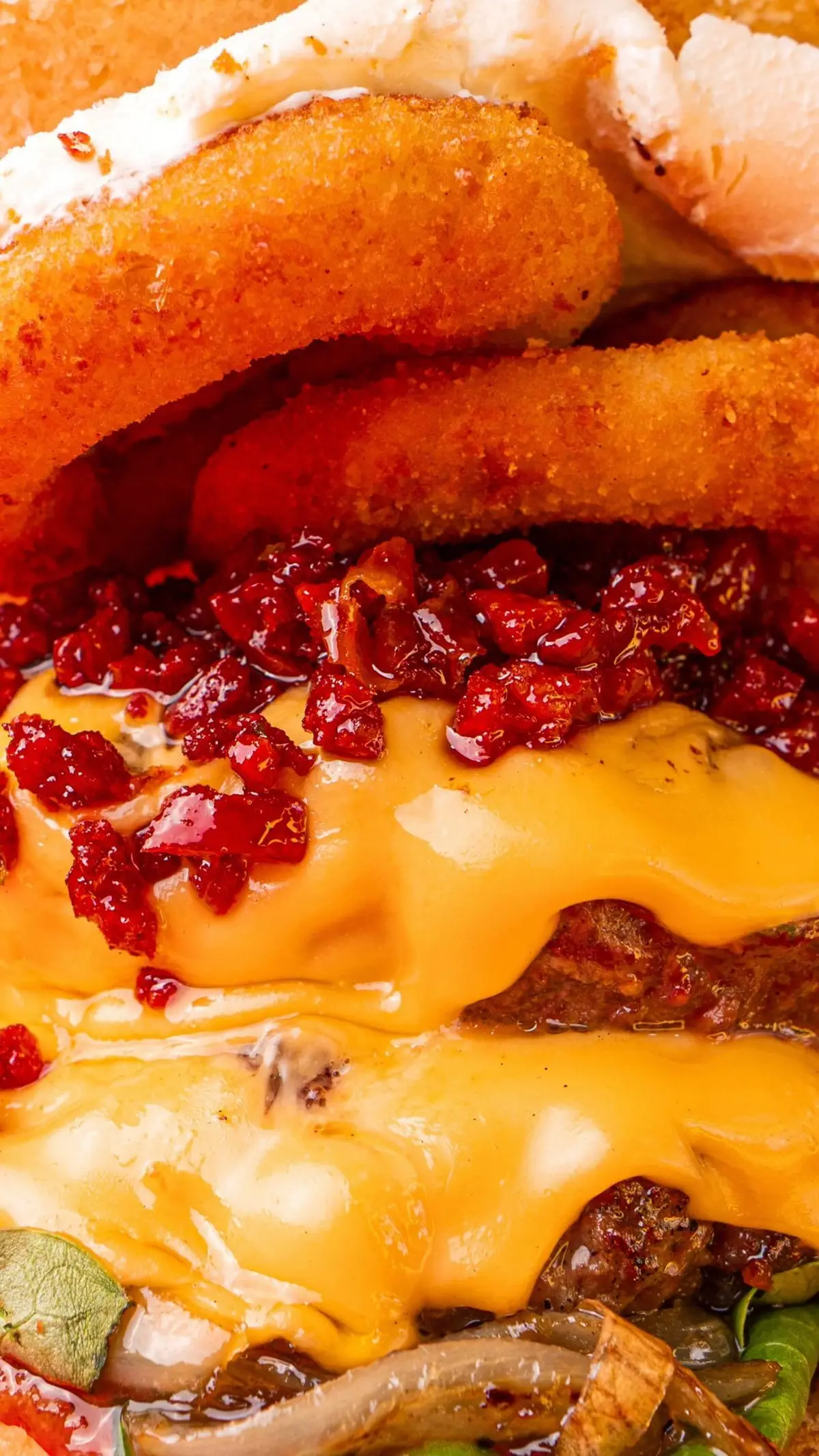 Primer plano de cheddar fundido, mermelada de chorizo y aros de cebolla sobre la carne