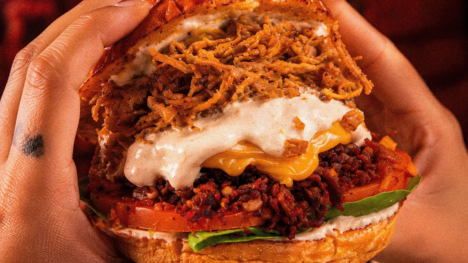 Burger Dakota sostenida en dos manos, con pulled pork, tocineta, cheddar y salsa de la casa